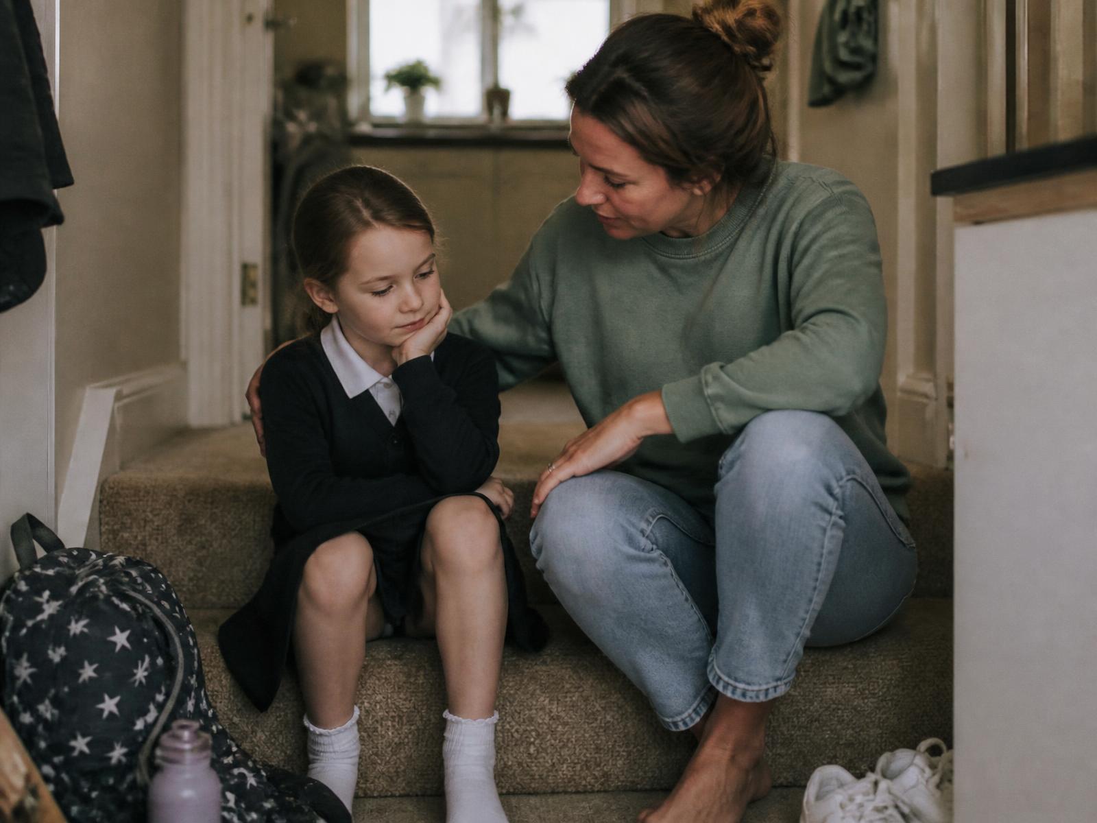 A mother sitting on the stairs with her daughter after school, listening quietly